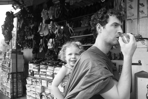 My three-year-old on her father's back in a sling while he enjoys chai at a market in Bangalore.