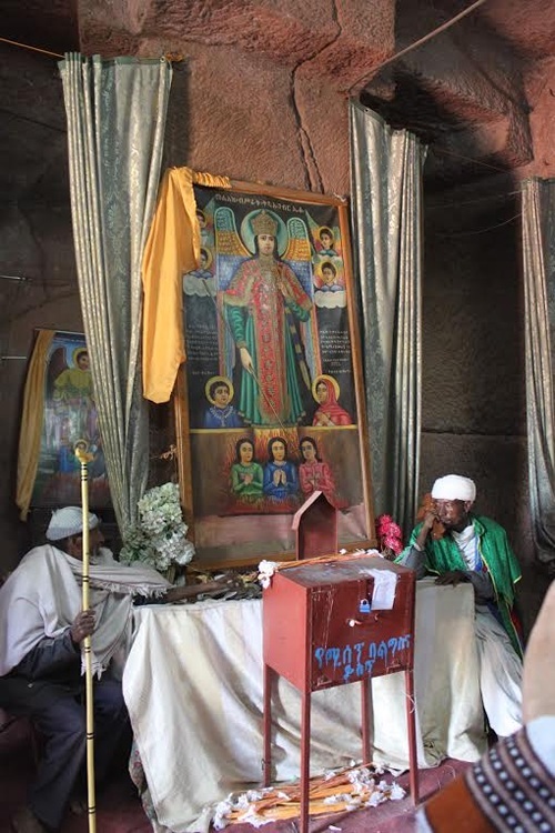 Priests in Ethiopia sitting on chairs at table with large icon at an altar.