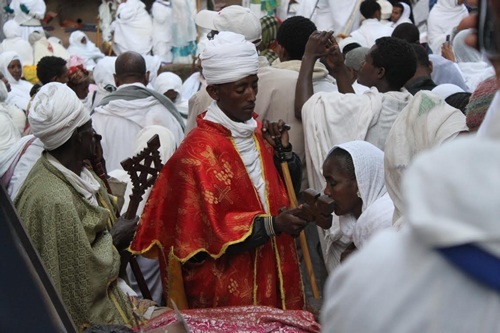 Priest in midst of procession in Lalibela, Ethiopia with worshipper kissing cross.