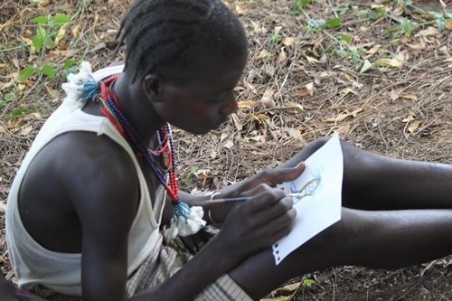 Ethiopia teen sitting and drawing on piece of paper.