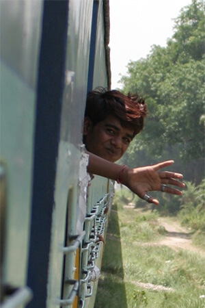 Boy waving hands outside window of Indian train.