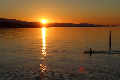 The sunset over Vancouver Island is spectacular as a man paddles a kayak.