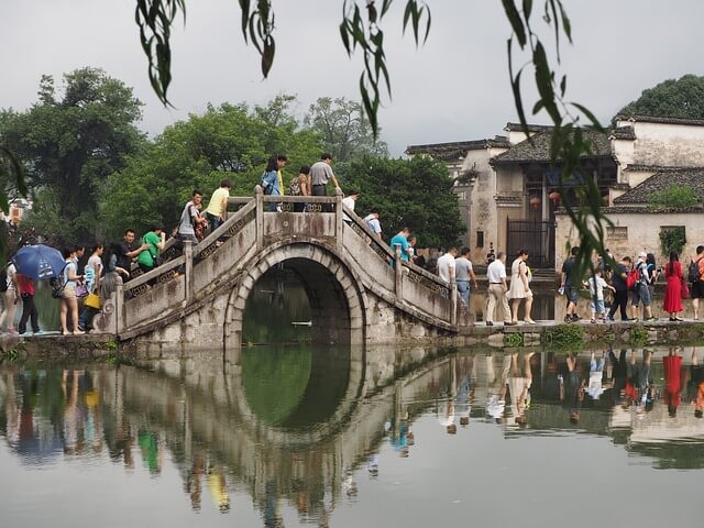 A small bridge in China with many people walking over to the other side.