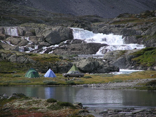 Camping in Europe with a car and tents near a rushing river.