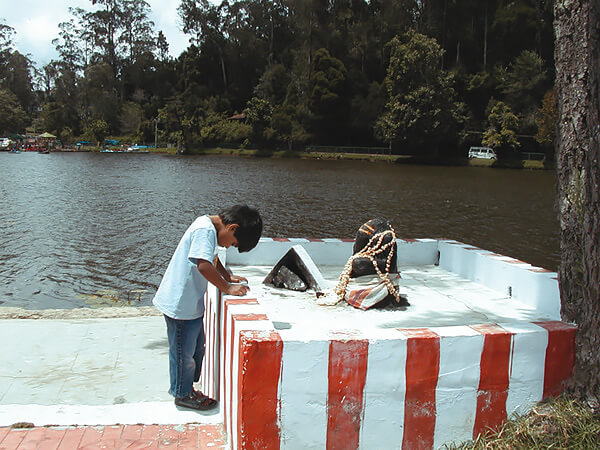 Little boy in prayer to the elephant-headed Hindu god Ganesh at a shrine by the water.