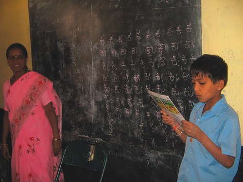 A child in India reading as his teacher looks on.